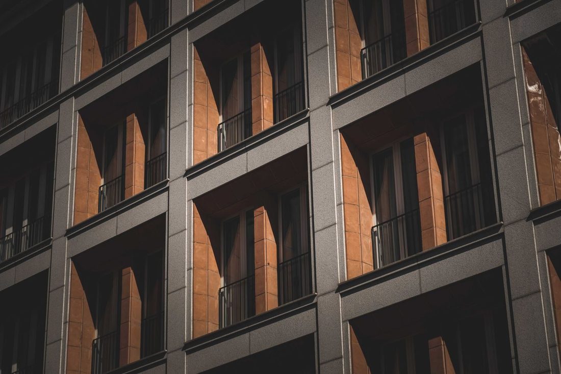 Low angle of symmetric windows windows with French balconies of modern multistory residential building on sunny day in city