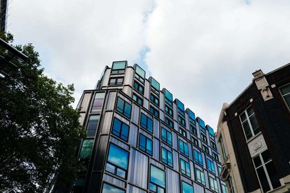 A contemporary building with reflective windows in an urban setting under a cloudy sky.