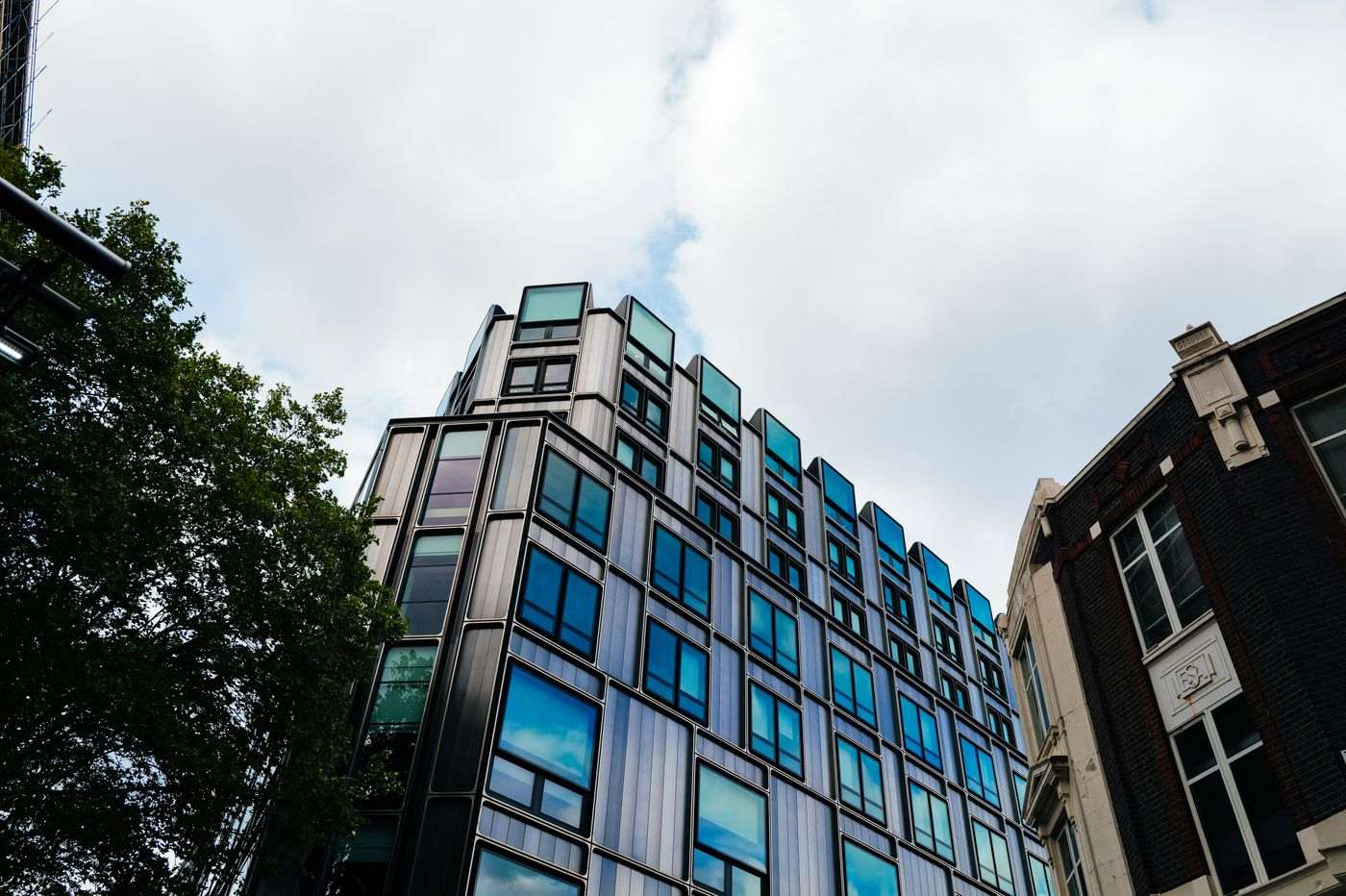 A contemporary building with reflective windows in an urban setting under a cloudy sky.