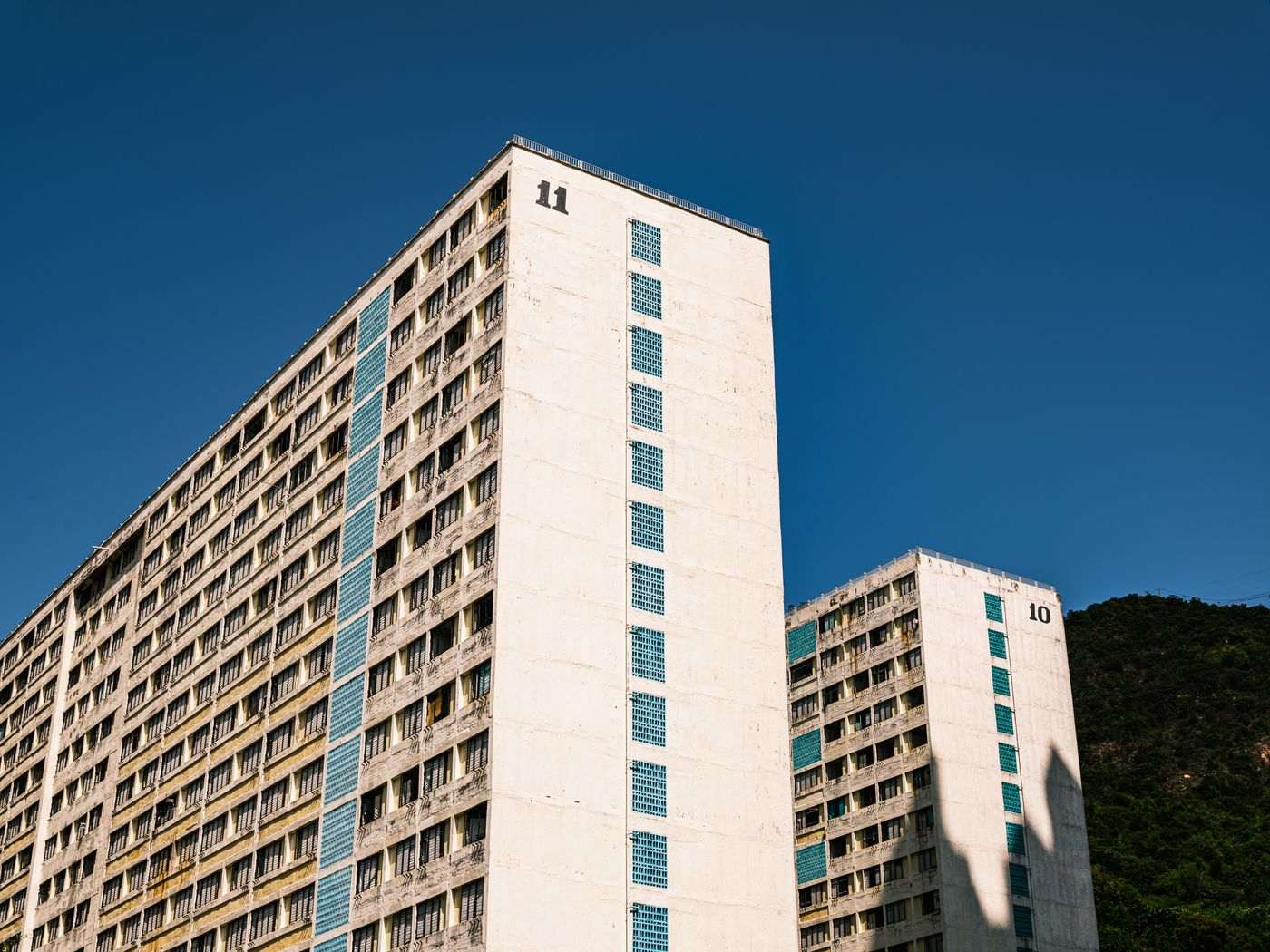 Low-angle view of two high-rise buildings under a clear blue sky with minimal cloud coverage.
