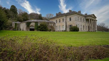 Elegant mansion surrounded by vibrant gardens and ivy-clad buildings.