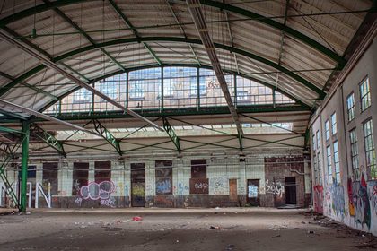 Interior of an abandoned warehouse with graffiti and debris, showcasing urban decay.