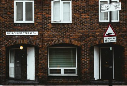 Facade of old brick residential building with plastic windows and jalousie near road with sign