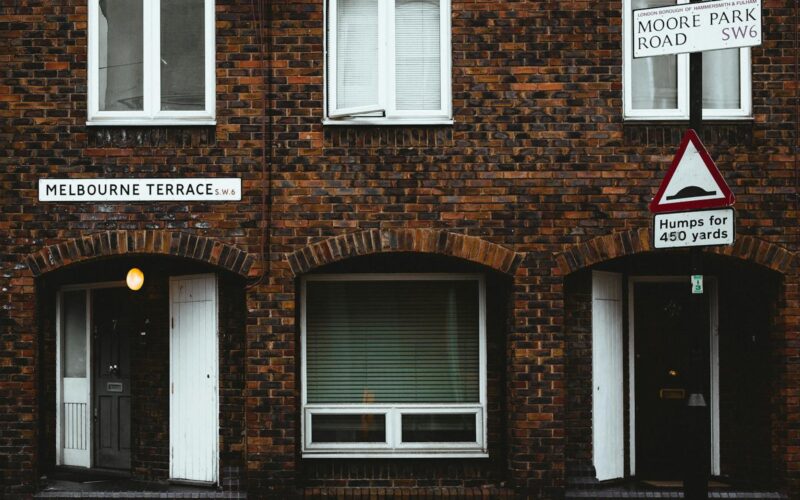 Facade of old brick residential building with plastic windows and jalousie near road with sign