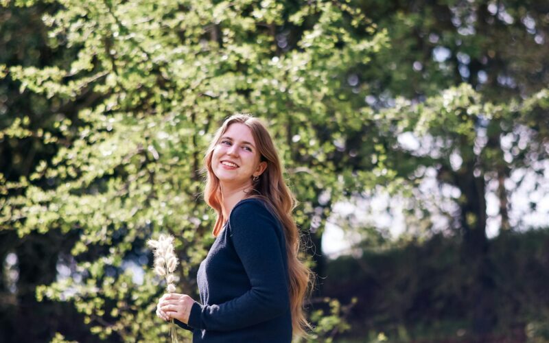 a woman standing in front of a tree holding a dandelion